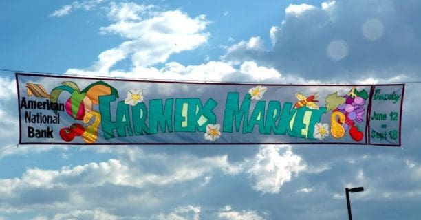 A banner that says farmers market with flowers on it.