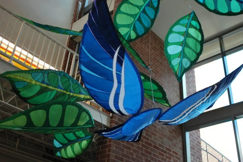 A blue bird flying through the air with leaves.