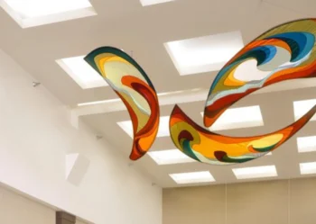 Three colorful abstract sculptures hang from the ceiling in a room with square recessed lights and beige walls.