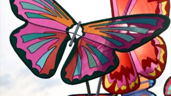 Close-up of colorful plastic butterfly decorations with pink, orange, teal, and purple patterns against a bright sky.