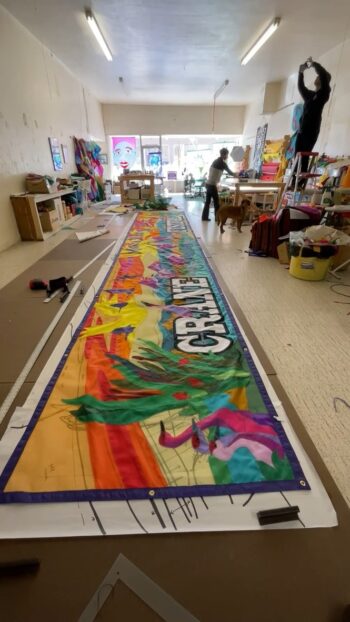 Large colorful mural on the floor of an art studio, with a person and dog working in the background.