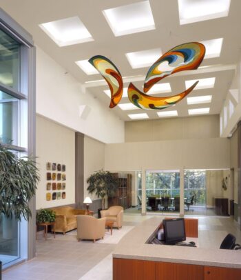 Modern office lobby with high ceilings, abstract art sculpture, seating area, desk, and large windows.
