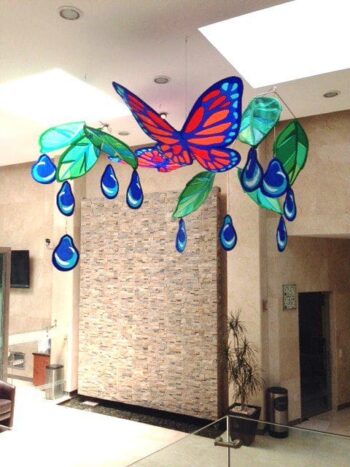 Hanging decoration of a large red and blue butterfly, green leaves, and blue droplets in a modern indoor space.