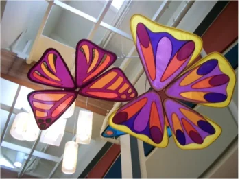 Two large, colorful butterfly decorations hang from a ceiling with white beams and pendant lights in the background.