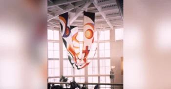 Three colorful abstract banners hang from a high ceiling in a bright, modern atrium with large windows.