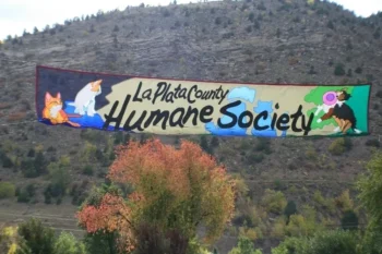 Banner reading "La Plata County Humane Society" with cartoon dog and cat, displayed outdoors in front of a rocky hillside.