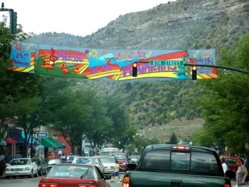 Colorful banner over a busy street advertises a music festival near a mountain, with cars and shops visible.