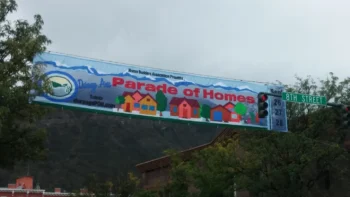 A parade banner for the Parade of Homes hangs over 8th Street, showing dates and colorful house illustrations.